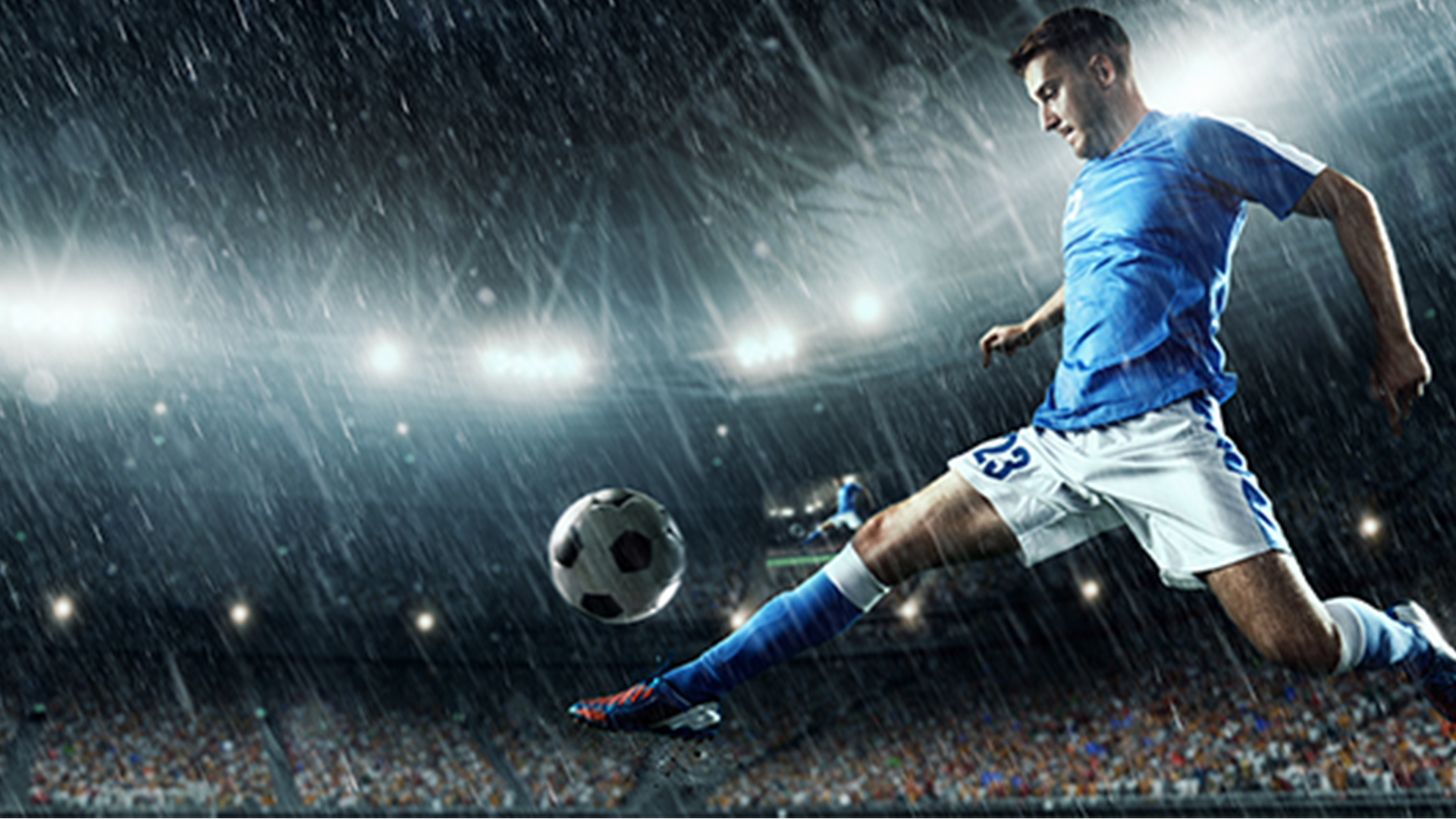Football player kicking a ball in a stadium during a rainy match.