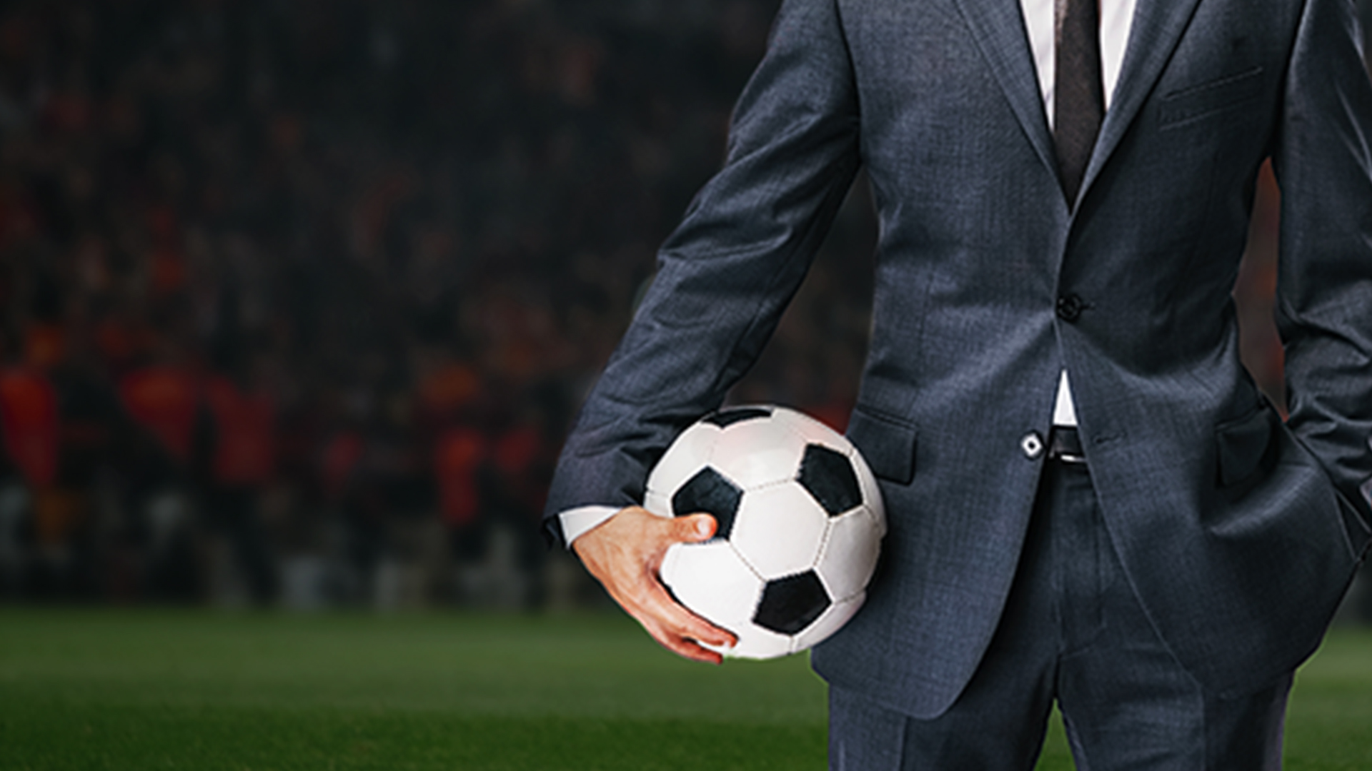 Man in suit holding a football on a pitch.
